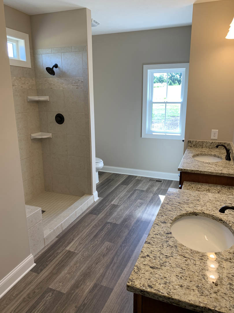 Marble countertop with undermount sink and chrome faucet, white framed window, bowl of milk on counter, walk-in shower with black shower head, large wall mirror, light tile