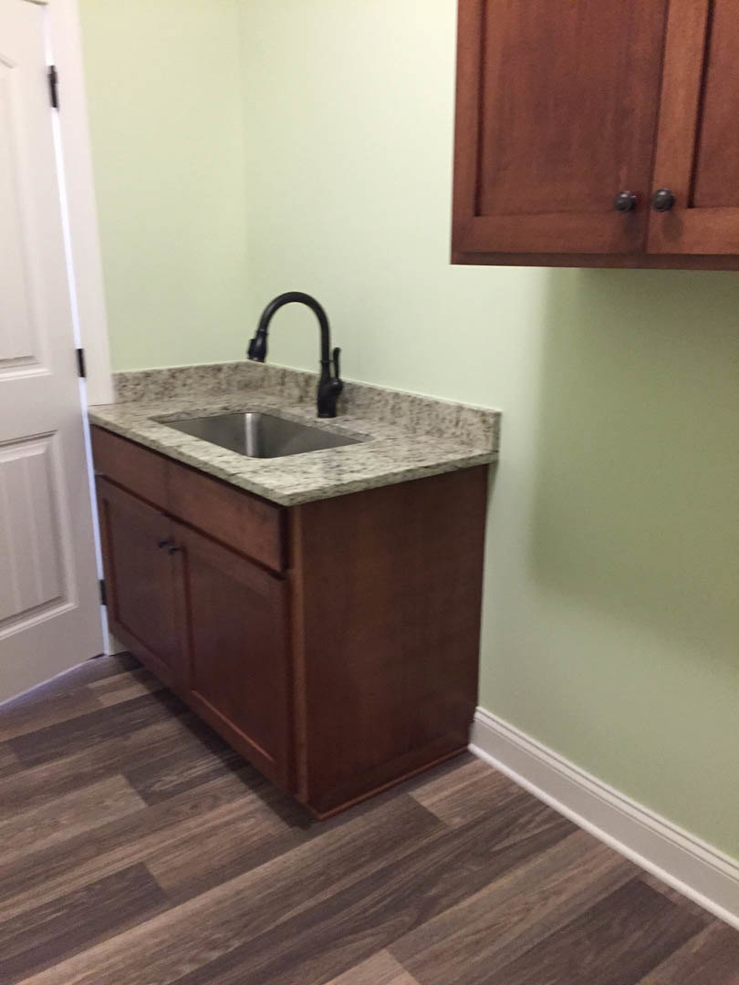 Undermount stainless steel sink with chrome faucet set in granite countertop, white shaker cabinets, wood flooring with white baseboard, white door, and black and white pendant