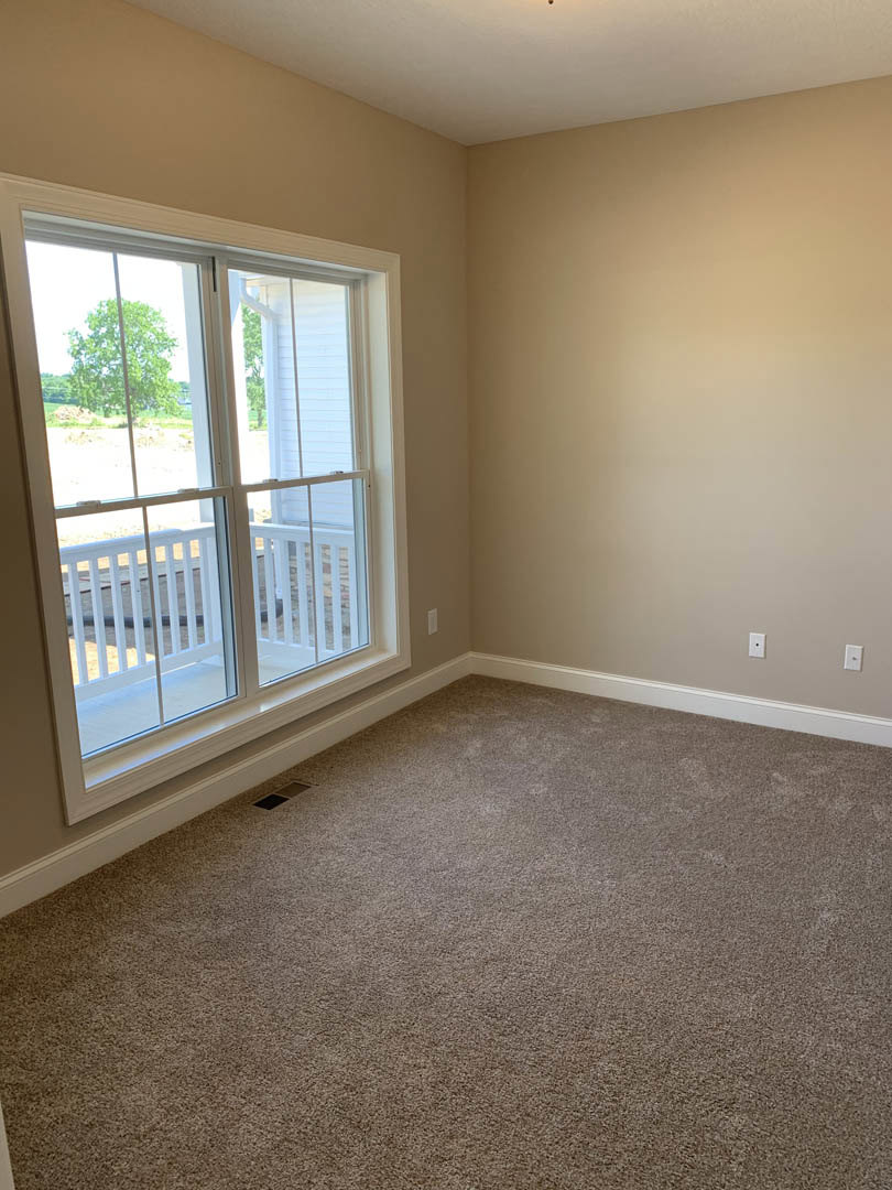 Carpeted room featuring a large window with white railing, plaster walls, and a sliding glass door with black trim.