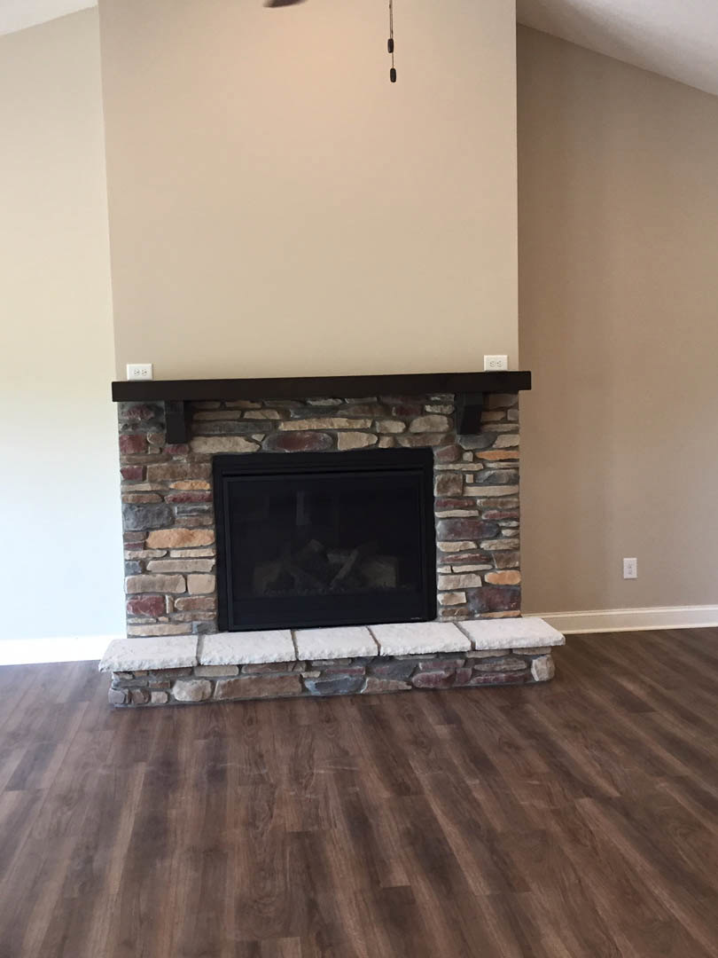 Stone fireplace with black-framed glass door set into white wall, wood flooring, and minimalist interior design
