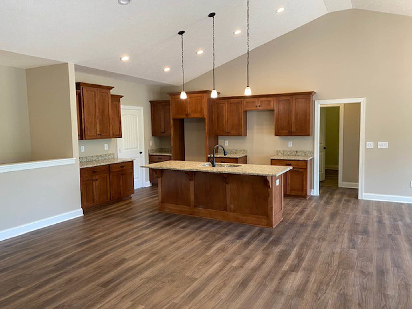 Kitchen with light wood flooring, white cabinetry, black hardware, stone countertop with built-in sink, and white door featuring a black handle.