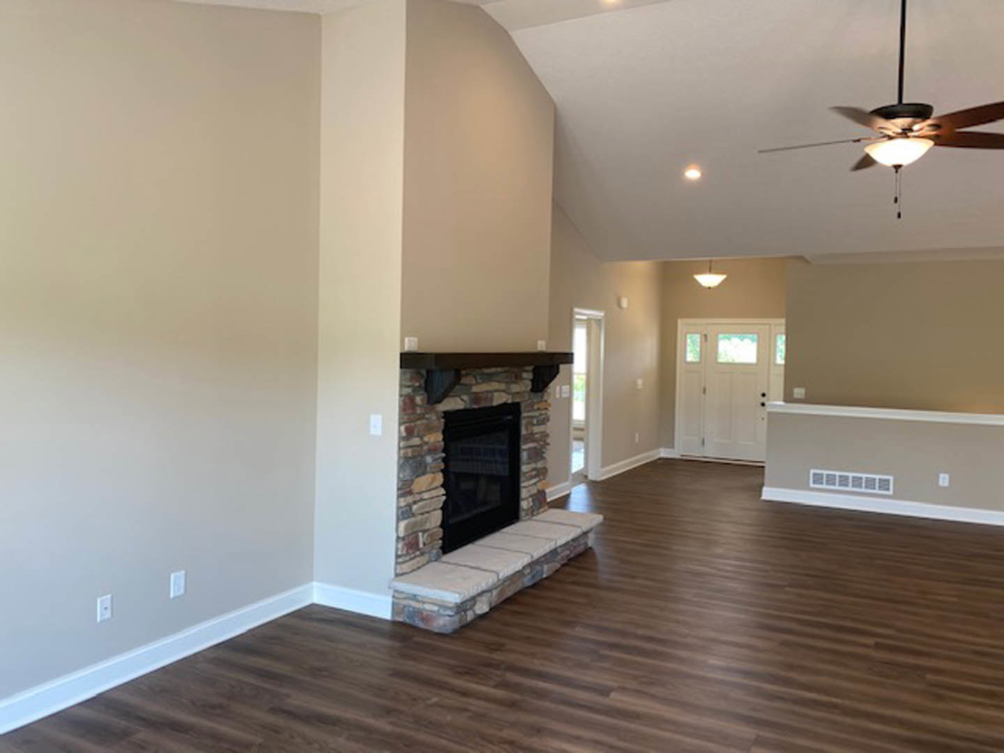 Living room with stone fireplace, black firebox, hardwood floors, white door with glass panes, neutral walls, and ceiling.
