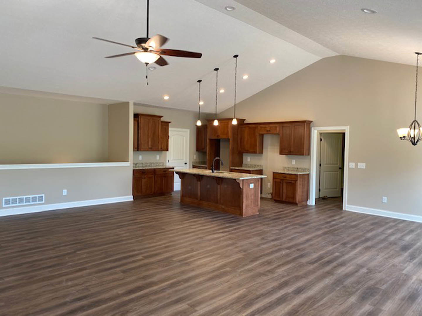 Spacious open floor plan featuring a kitchen island with marble countertop, wood flooring, white cabinetry, ceiling fan with light fixture, and a white door with black handle