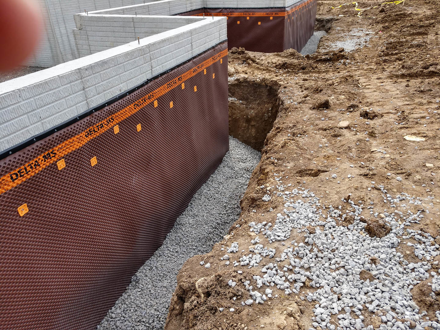 Concrete foundation with exposed rebar grid, surrounded by dirt, rocks, and construction materials at an outdoor building site