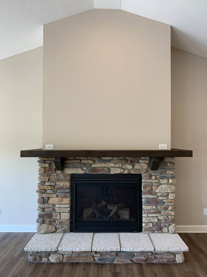 Stone fireplace with white tile surround, wood pile stacked on hearth, white ceiling and wall, fire screen in front of firebox, hardwood floor.