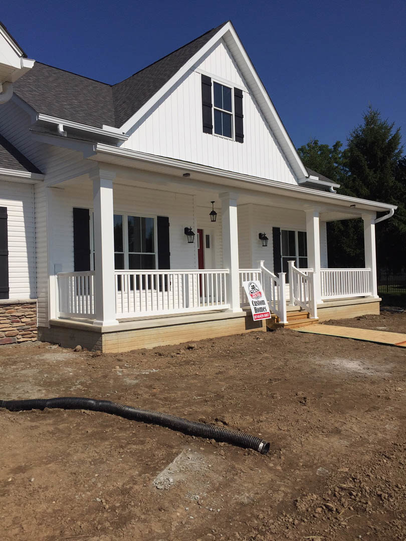 White house with horizontal siding, front porch, rectangular window, black pipe lying on ground, and a sign displayed near entry steps