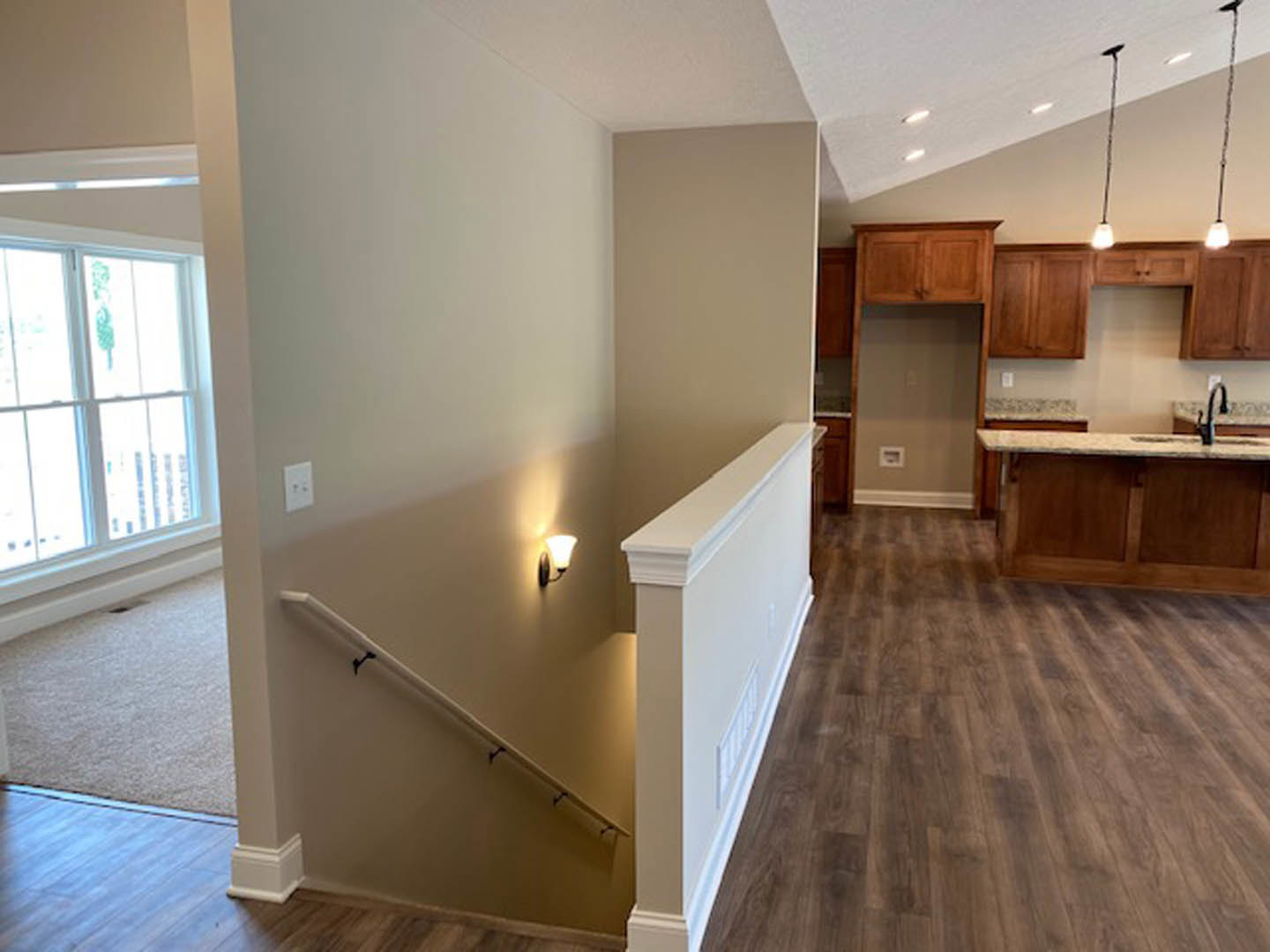 Wood staircase with white risers and baseboard, marble kitchen countertop, white cabinetry, wood flooring, window with green and white sign, doorway leading to adjacent room