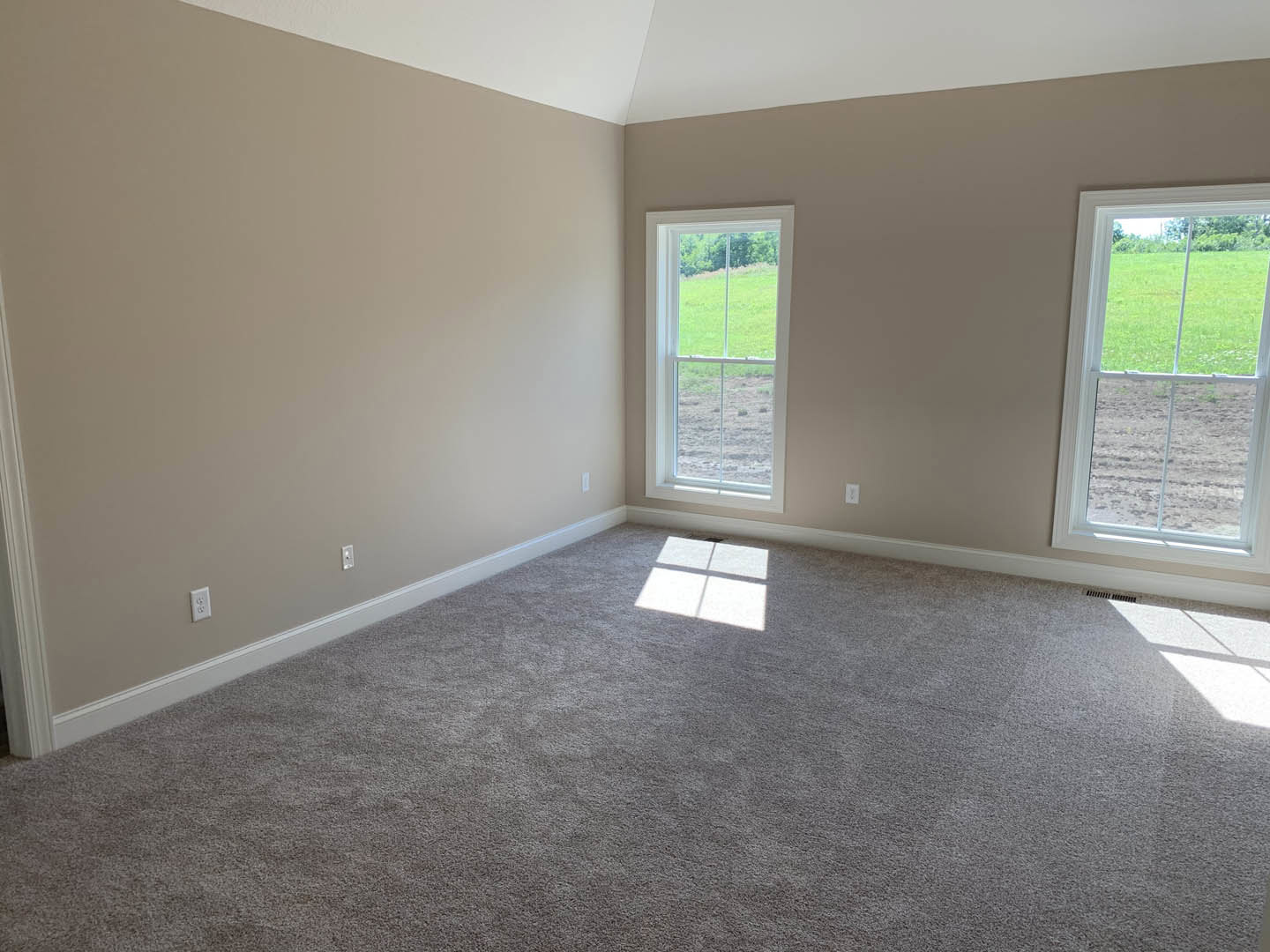 Carpeted room with two large windows, white walls, and view of green field outside