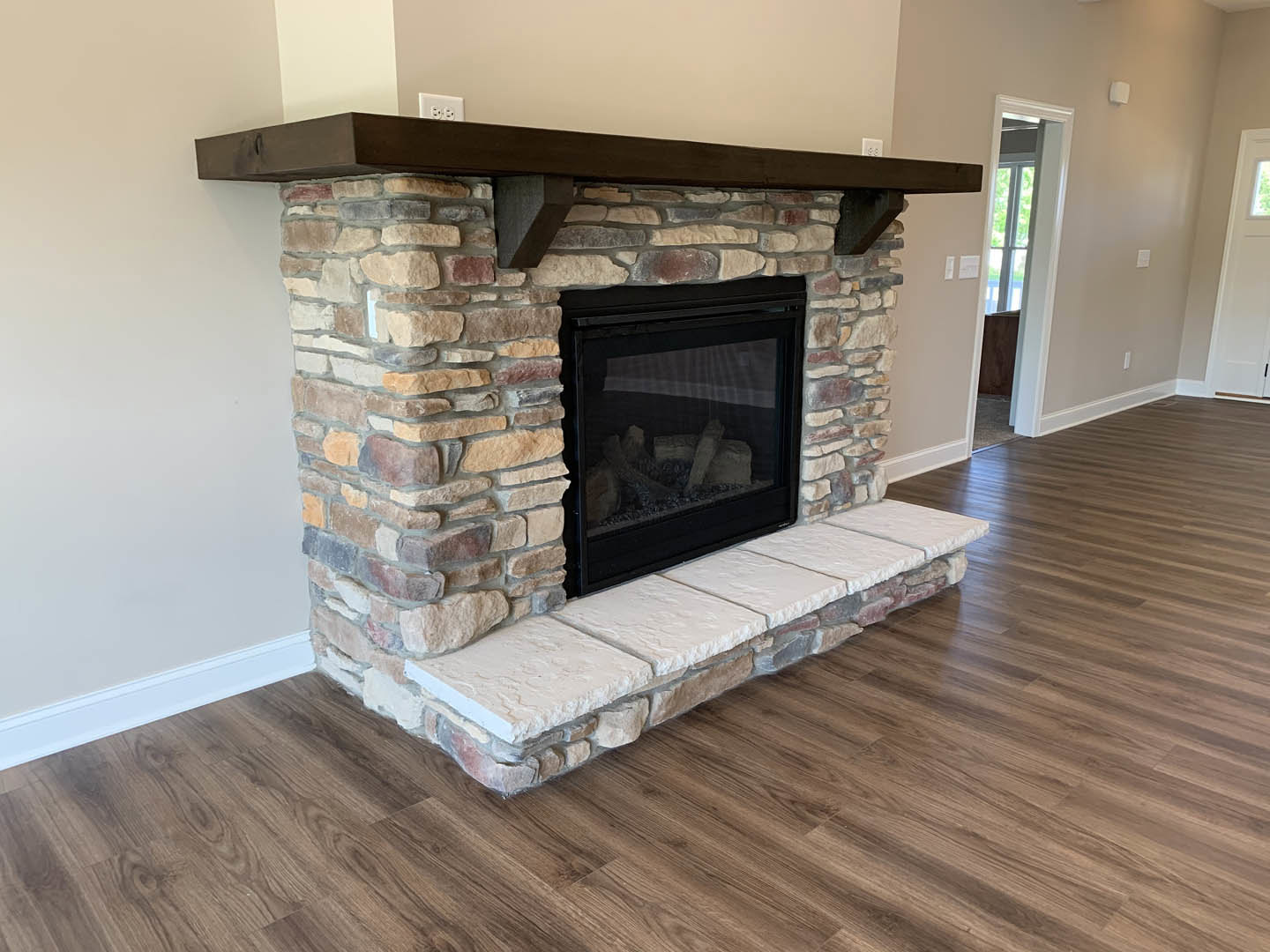 Stone fireplace with glass door and wood mantle, flanked by stone pillars, set on hardwood floor in a cozy room