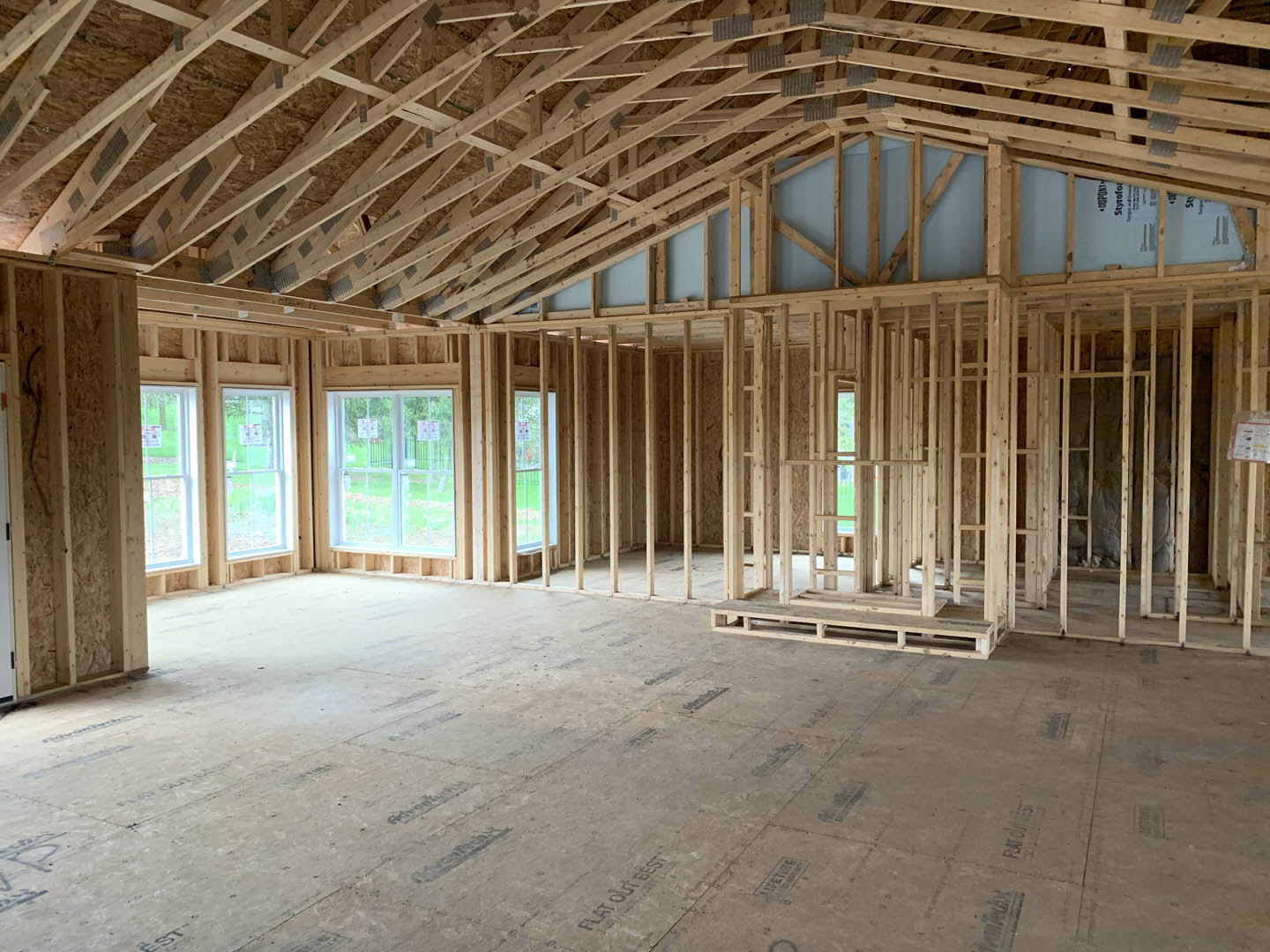 Living room with exposed wood ceiling beams, large windows, light hardwood floors, and a paper sign taped to one window.