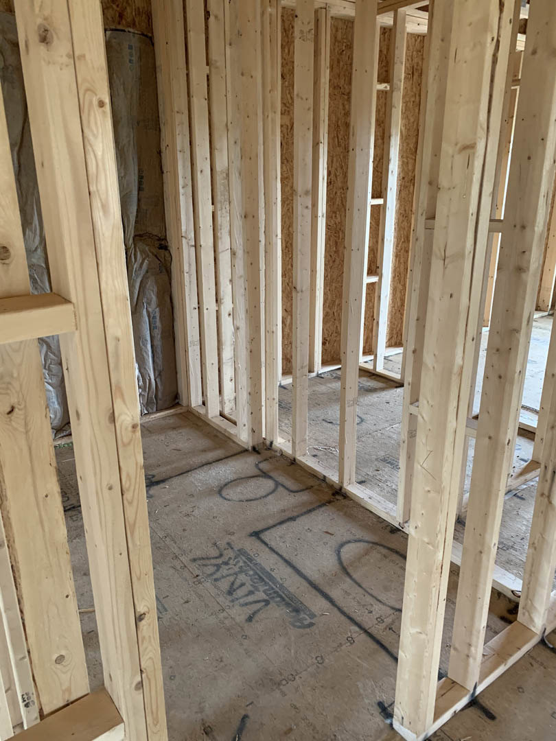Exposed wood framing and beams in a partially constructed room with a concrete floor marked by black writing