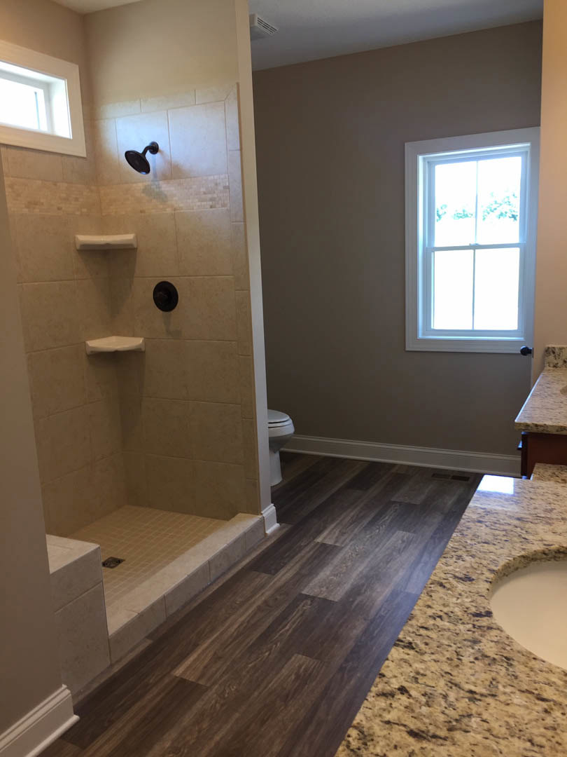 Modern bathroom featuring a glass-enclosed shower, white framed window, light stone countertop with vessel sink, matte black wall-mounted faucet, and neutral tile flooring.