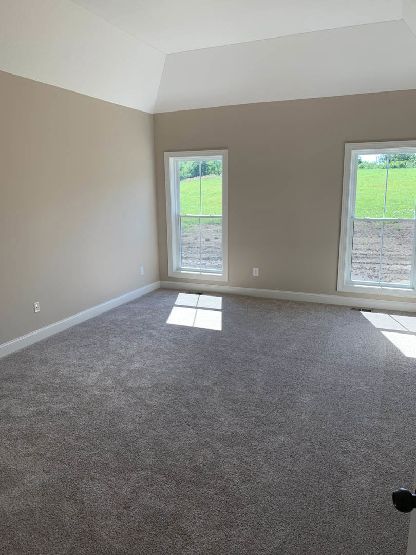 Carpeted room featuring large windows with views of a green field, white walls, and window blinds