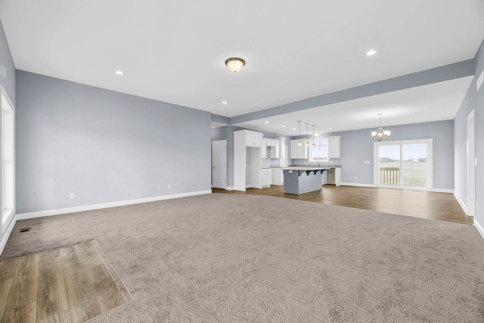 Open-concept kitchen and dining area with wood flooring, patterned rug, white cabinetry, modern light fixture, and large window overlooking a grassy field