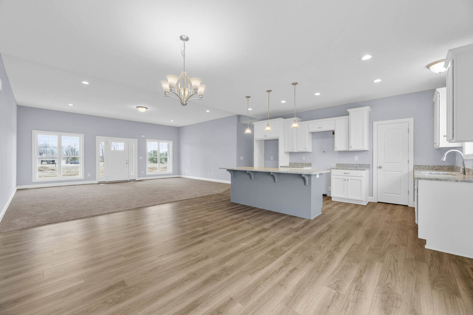 Spacious kitchen with central island, hardwood flooring, white cabinetry, stainless steel sink, white door with glass panels, large window overlooking parking lot