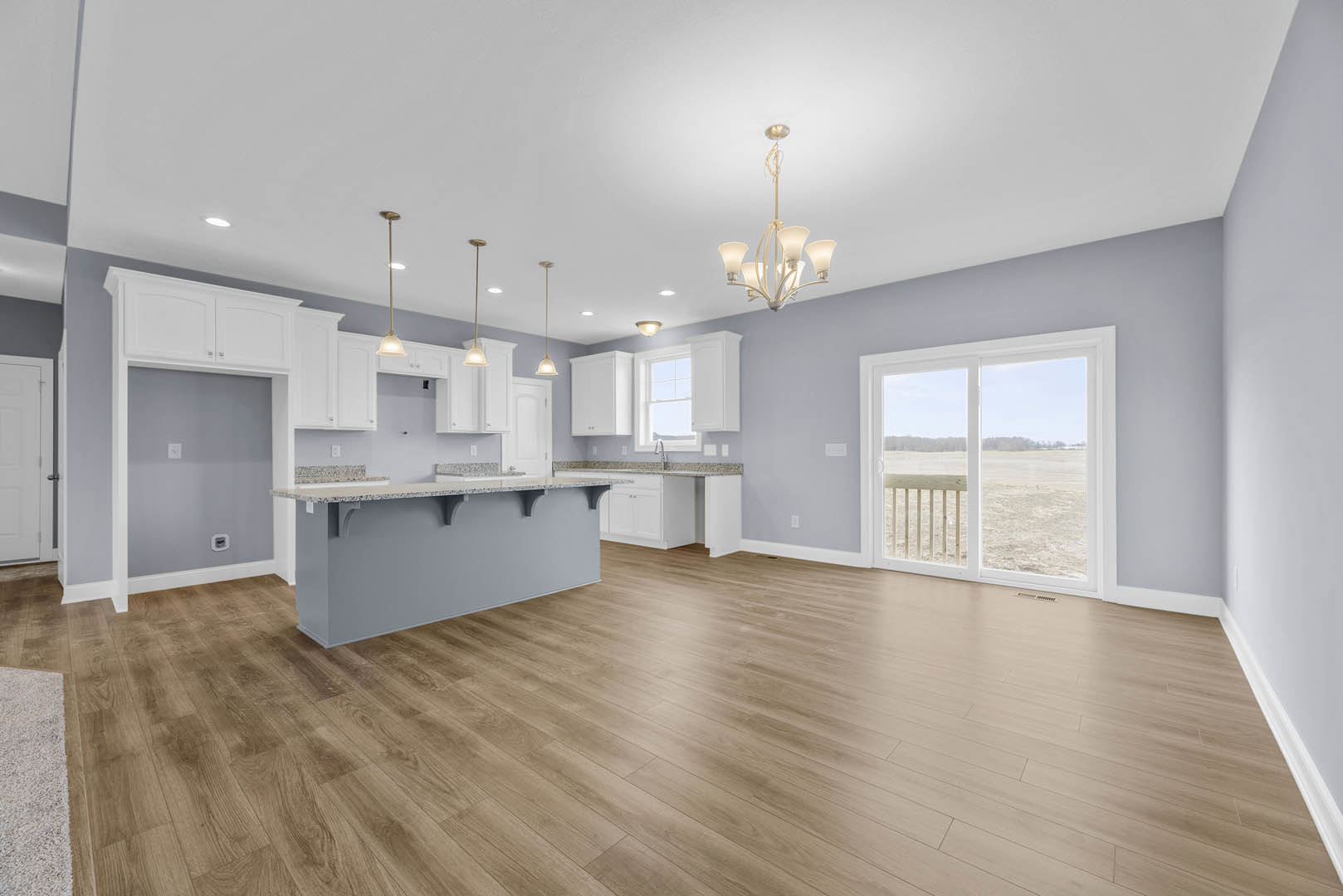 Open-concept kitchen and living room featuring hardwood floors, white cabinetry, stone countertop, sliding glass door overlooking a grassy field, modern chandelier, and neutral