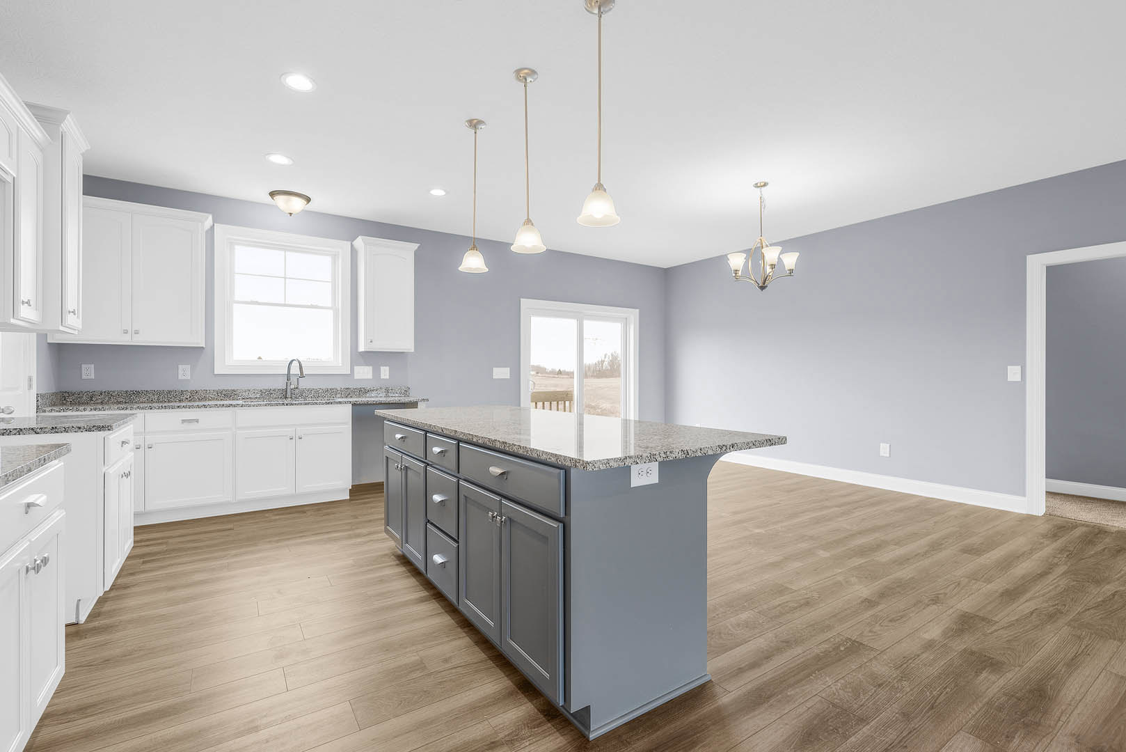 Spacious kitchen featuring a large island with marble countertops, multiple drawers, stainless steel sink beneath a window overlooking a field, white cabinetry, and a chandelier