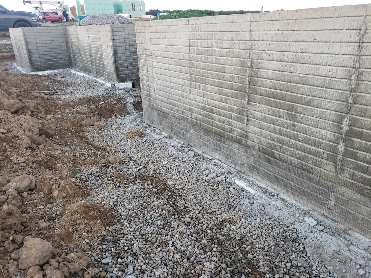 Concrete exterior wall bordered by gravel and dirt, with scattered rocks and bricks visible along the ground.