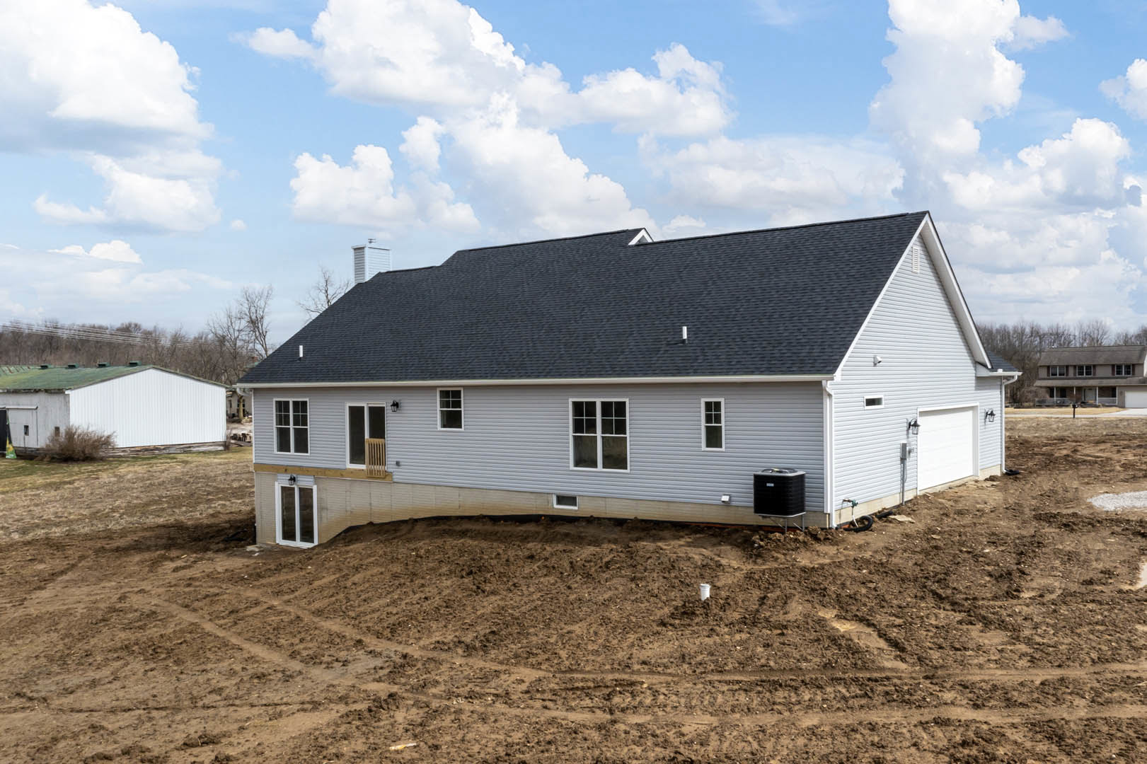 Partially built white house with green roof, exposed framing, dirt lot in foreground, scattered construction materials, blue sky with clouds overhead