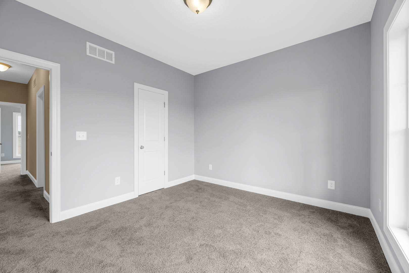 White paneled door with silver knob, beige carpet flooring, wall vent, ceiling-mounted light fixture, white plaster walls with crown molding