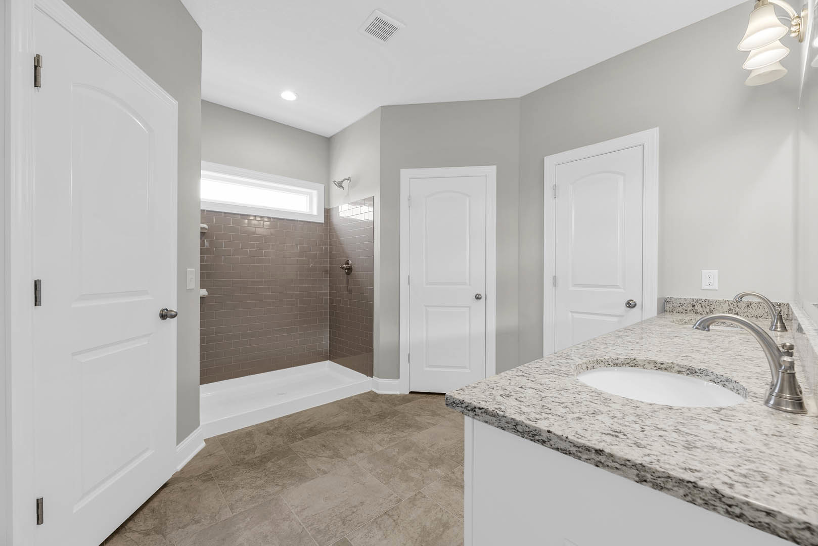 Bathroom featuring a marble countertop with undermount sink and chrome faucet, glass-enclosed shower with tiled walls, white door with silver knob, and modern light fixture.