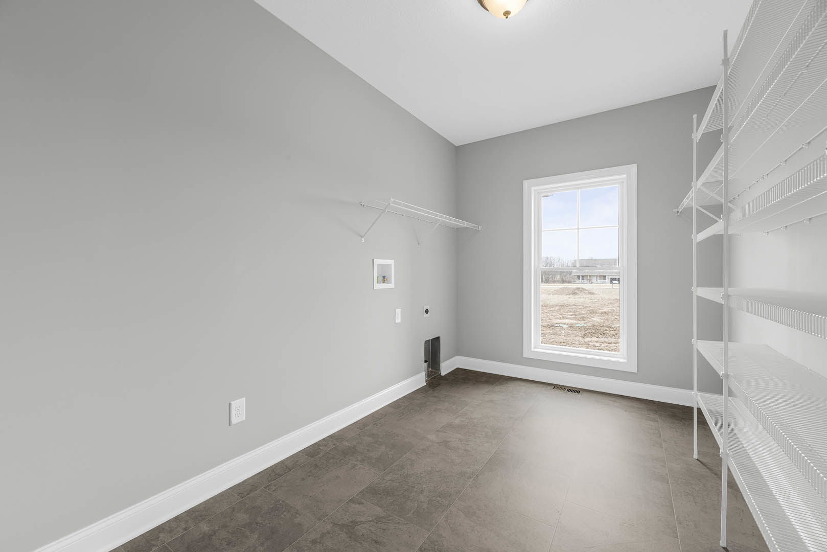 Grey tile floor with white baseboard, white metal shelving, large glass window in white frame overlooking a field, plaster walls, ceiling light fixture