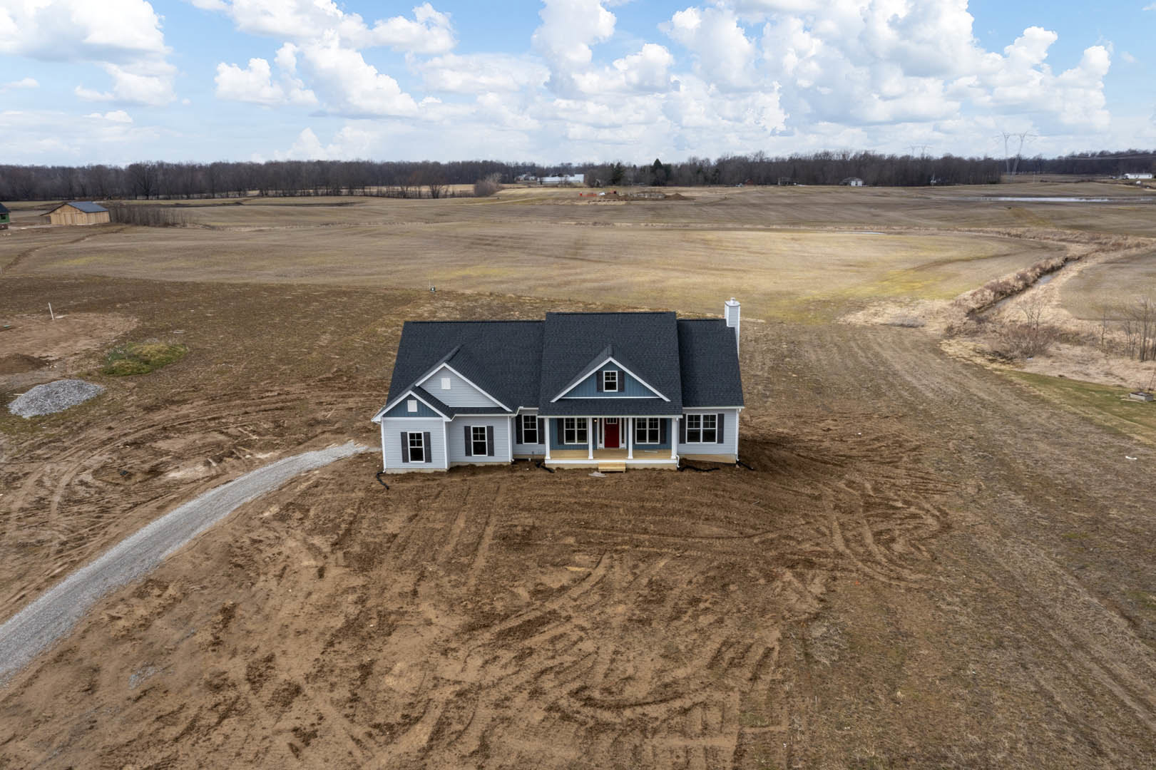 Blue-roofed house with white-trimmed windows set in a grassy field under a partly cloudy sky, grey rock visible in foreground