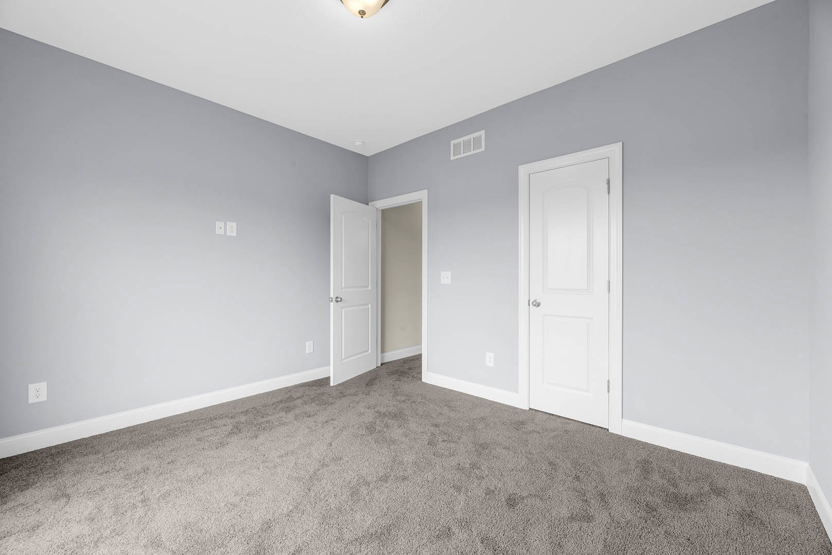 Carpeted room with two white doors featuring silver knobs, white walls with matching trim, and a wall vent.