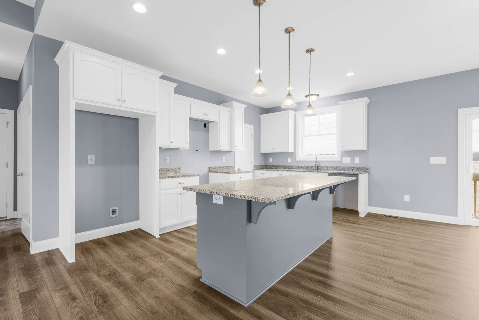 Marble kitchen island with waterfall edge, pendant lights above, white cabinetry, stainless steel sink, light wood flooring, and smooth stone countertops