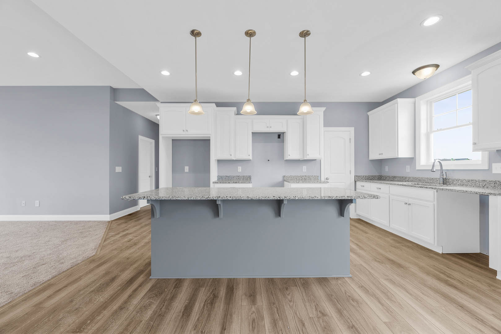 Marble kitchen island with waterfall edge, wood flooring, white cabinetry, tile backsplash, stainless steel sink, and recessed ceiling lighting