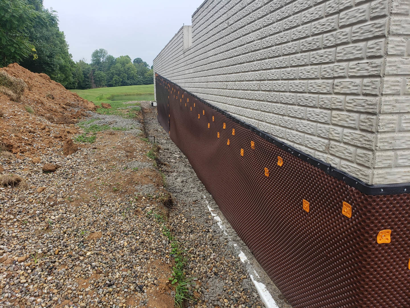 White brick exterior wall featuring brown and orange dot pattern, with grassy ground and trees under a cloudy sky