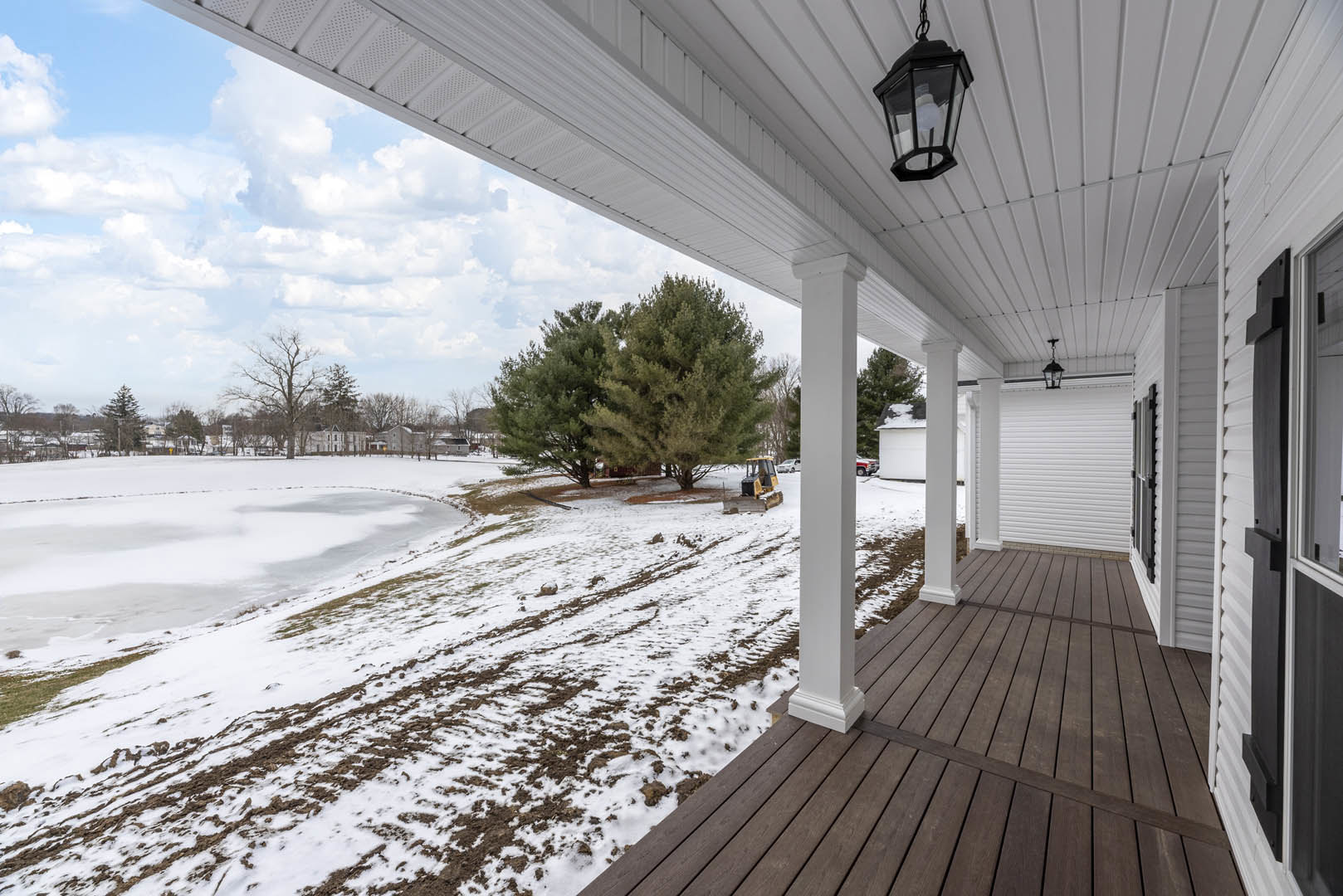 Wooden porch with white pillars overlooking snow-covered ground and leafless trees, winter sky in background