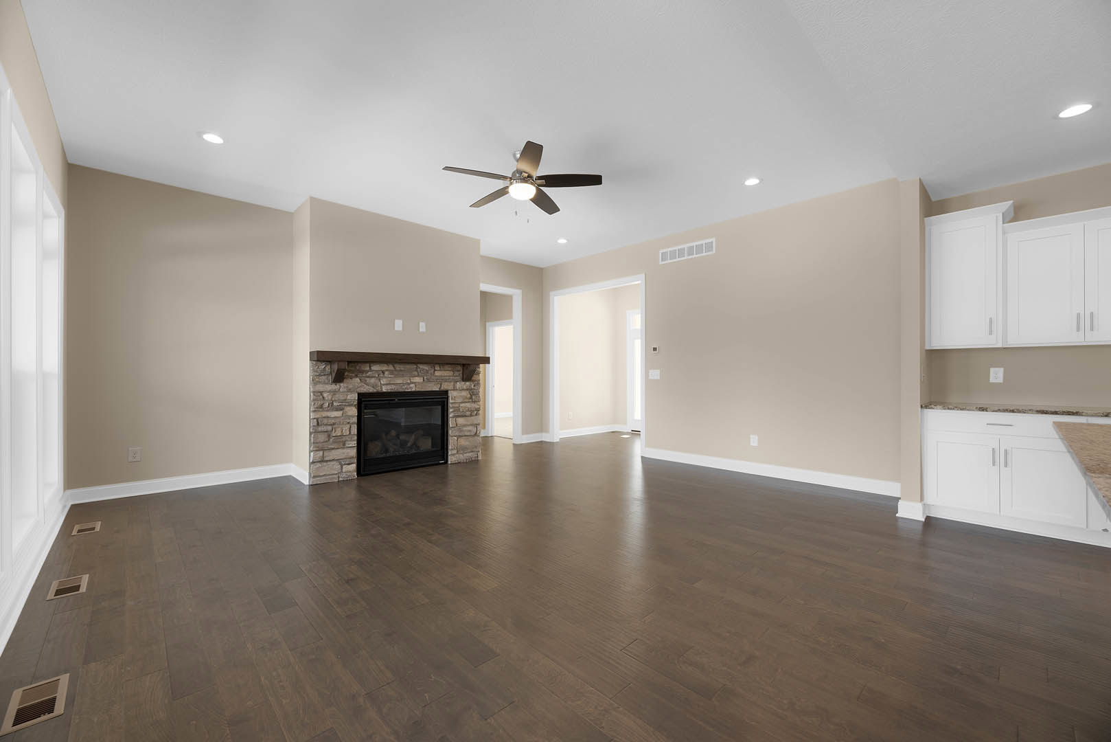 Living room with hardwood flooring, white cabinetry, glass-door fireplace burning wood, and ceiling fan with light fixture