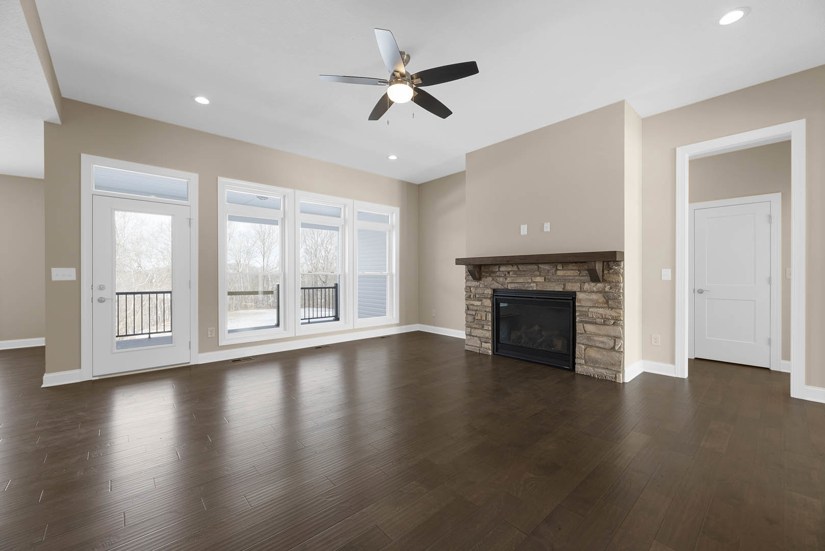 Living room with stone fireplace featuring glass doors, wood laminate flooring, ceiling fan with light, and white door with silver handle