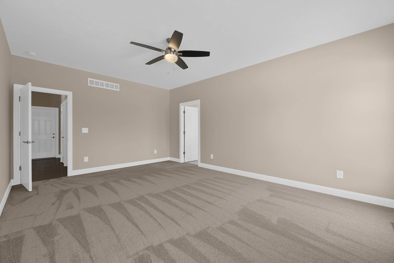 Carpeted room with white walls, ceiling fan with light fixture, open white door with metal handle leading to hallway