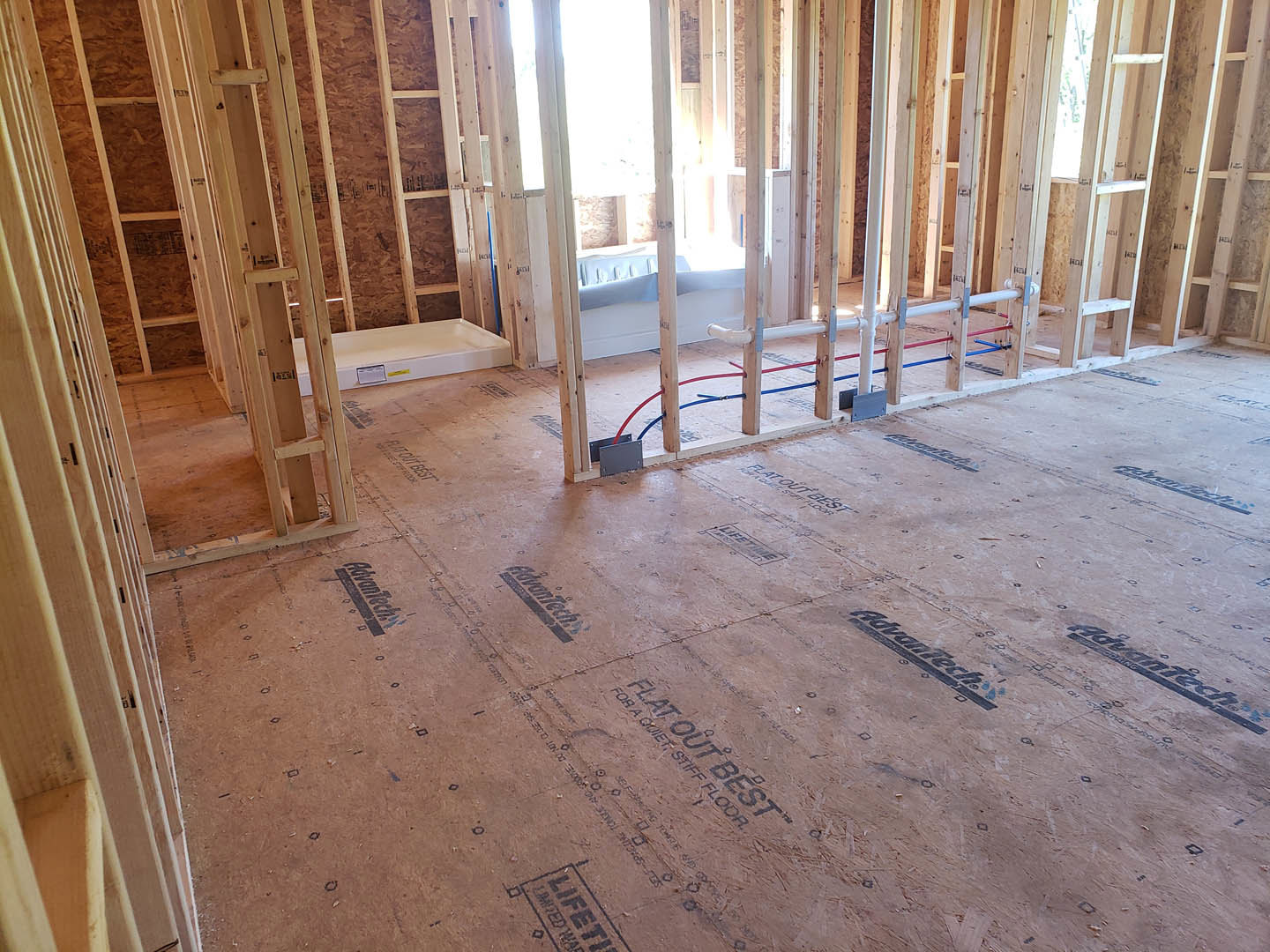 Wood-framed room under construction with exposed pipes, wiring, and a window