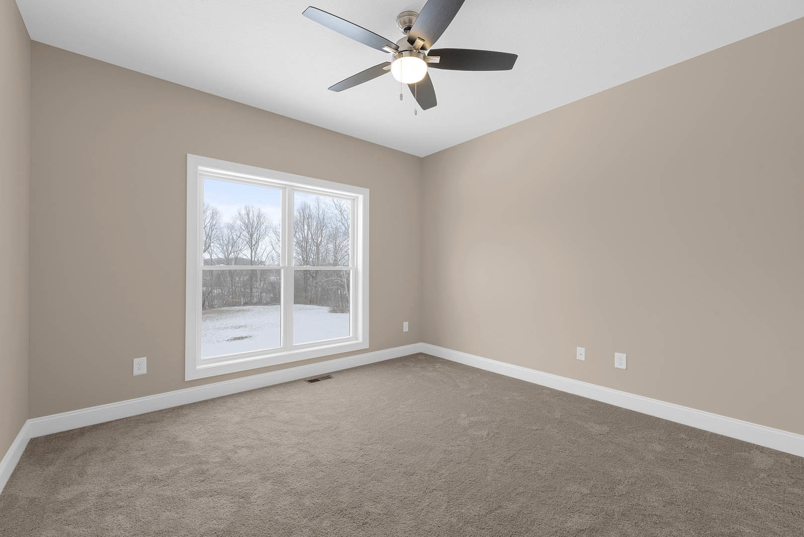 Carpeted room with white walls, ceiling fan with light fixture, large window overlooking snowy field and trees