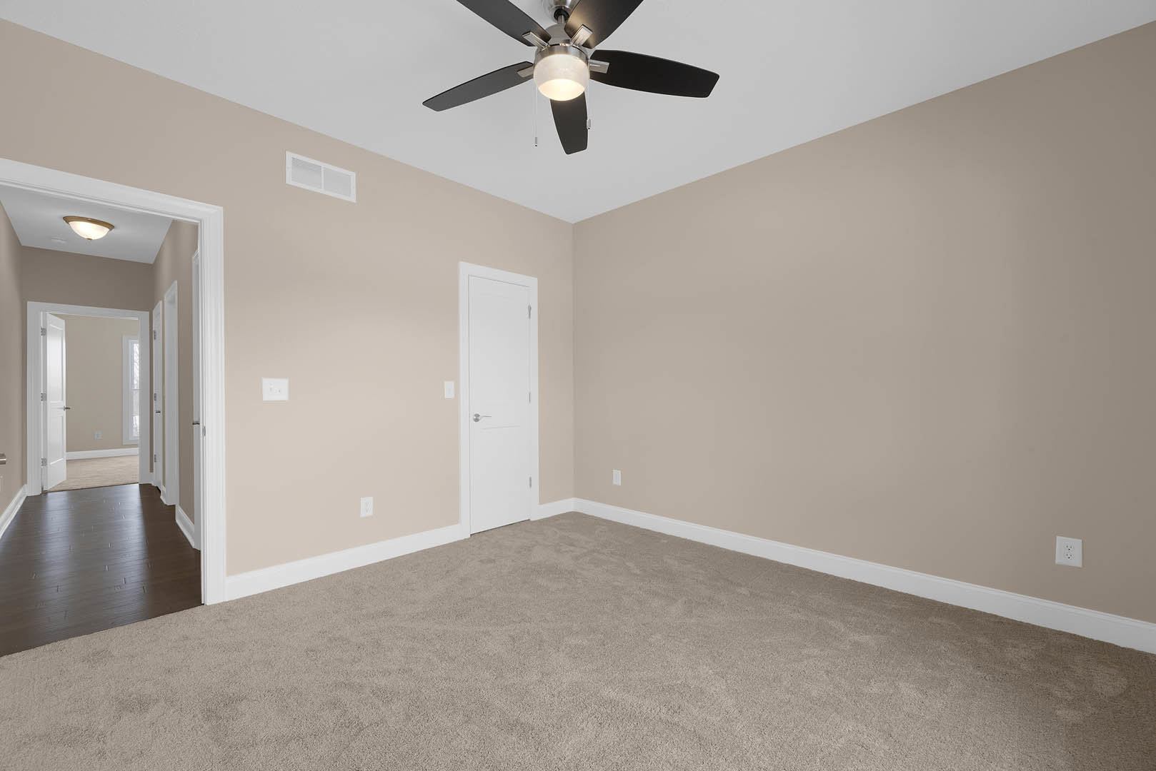 Ceiling fan with light fixture mounted above dark wood flooring and white carpet, white door with silver handle, plaster walls and ceiling