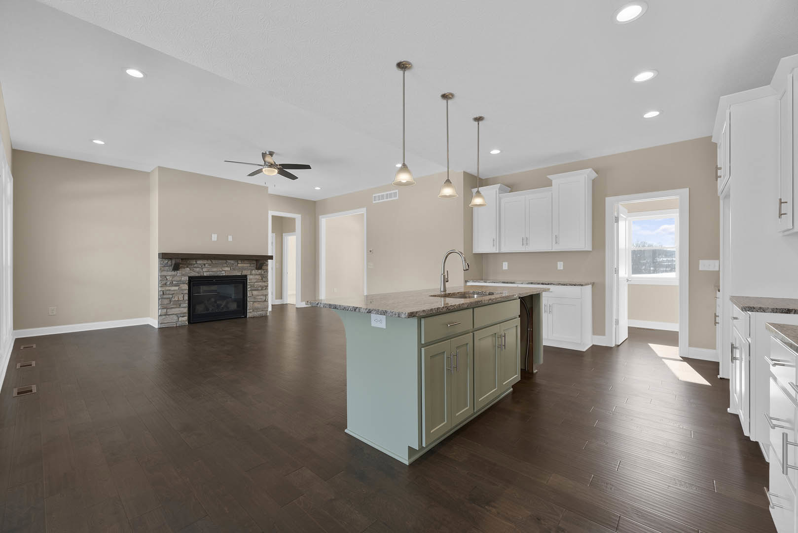 Open-concept kitchen and living room featuring a black glass-door fireplace, ceiling fan with light, kitchen island with granite countertops and sink, white door with window, wood
