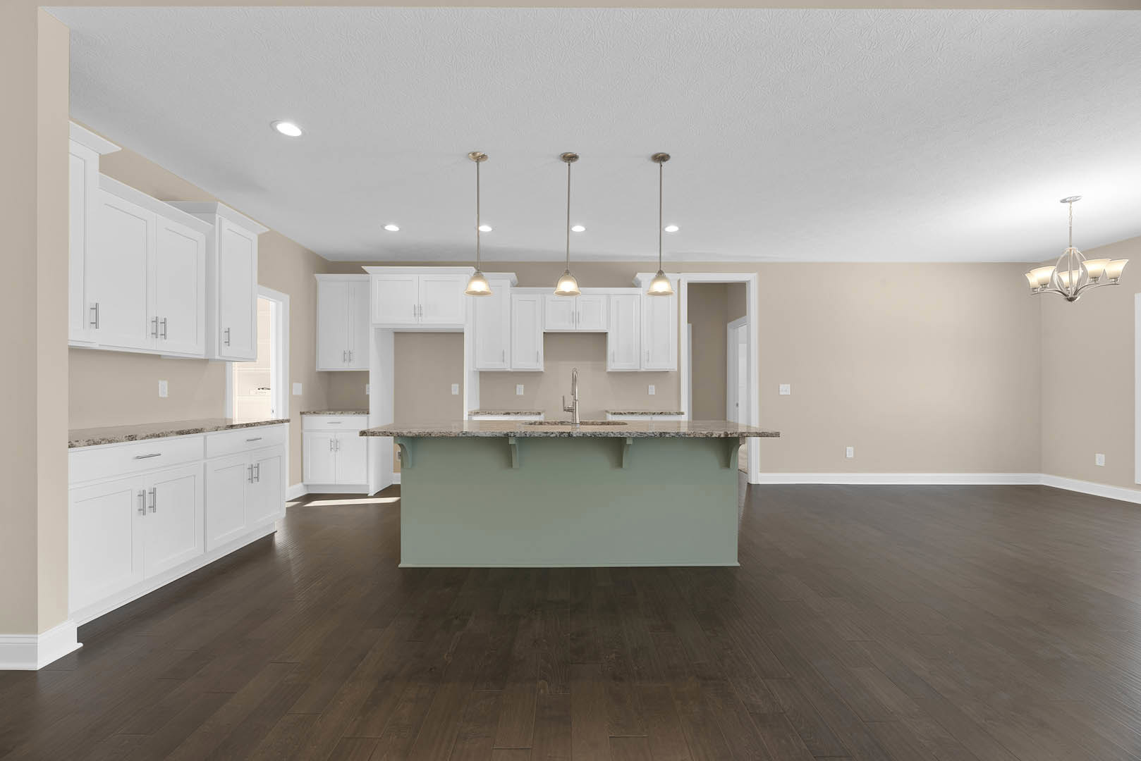 White kitchen cabinets with silver handles, central island with built-in sink, wood flooring, white walls, and a ceiling light fixture with four shades