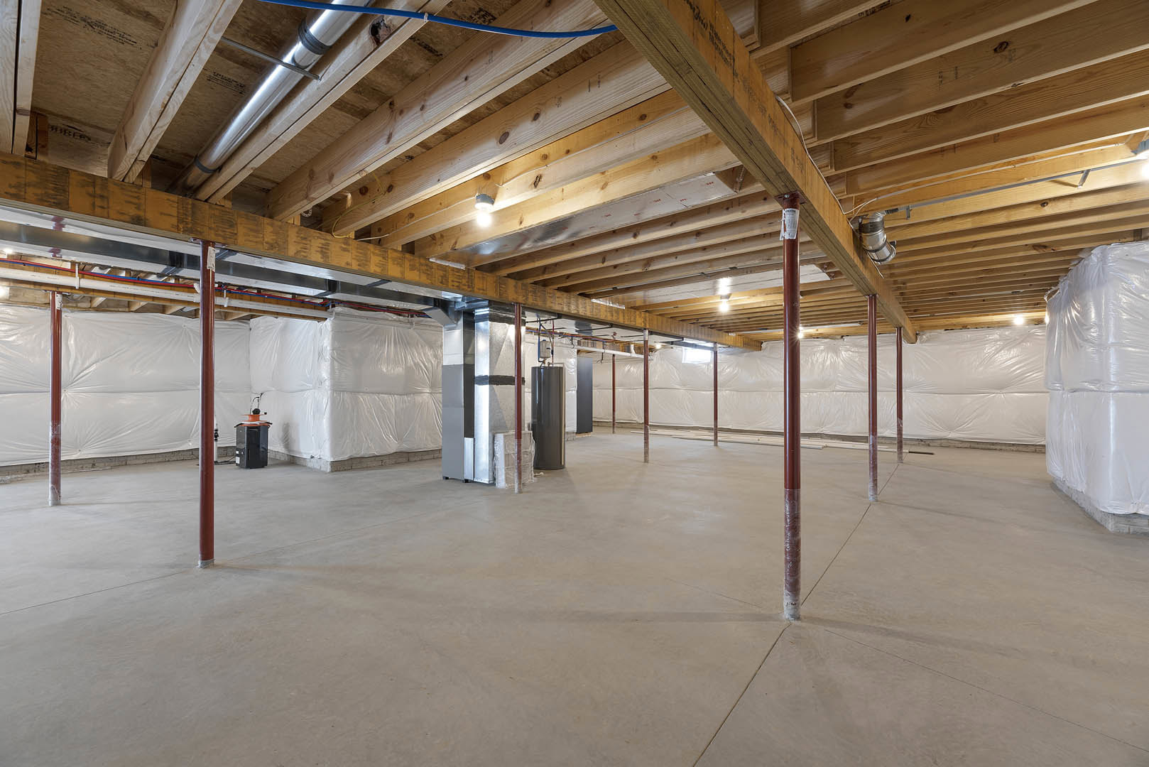 Exposed wooden ceiling beams and metal pipes above a concrete floor with a steel support pole