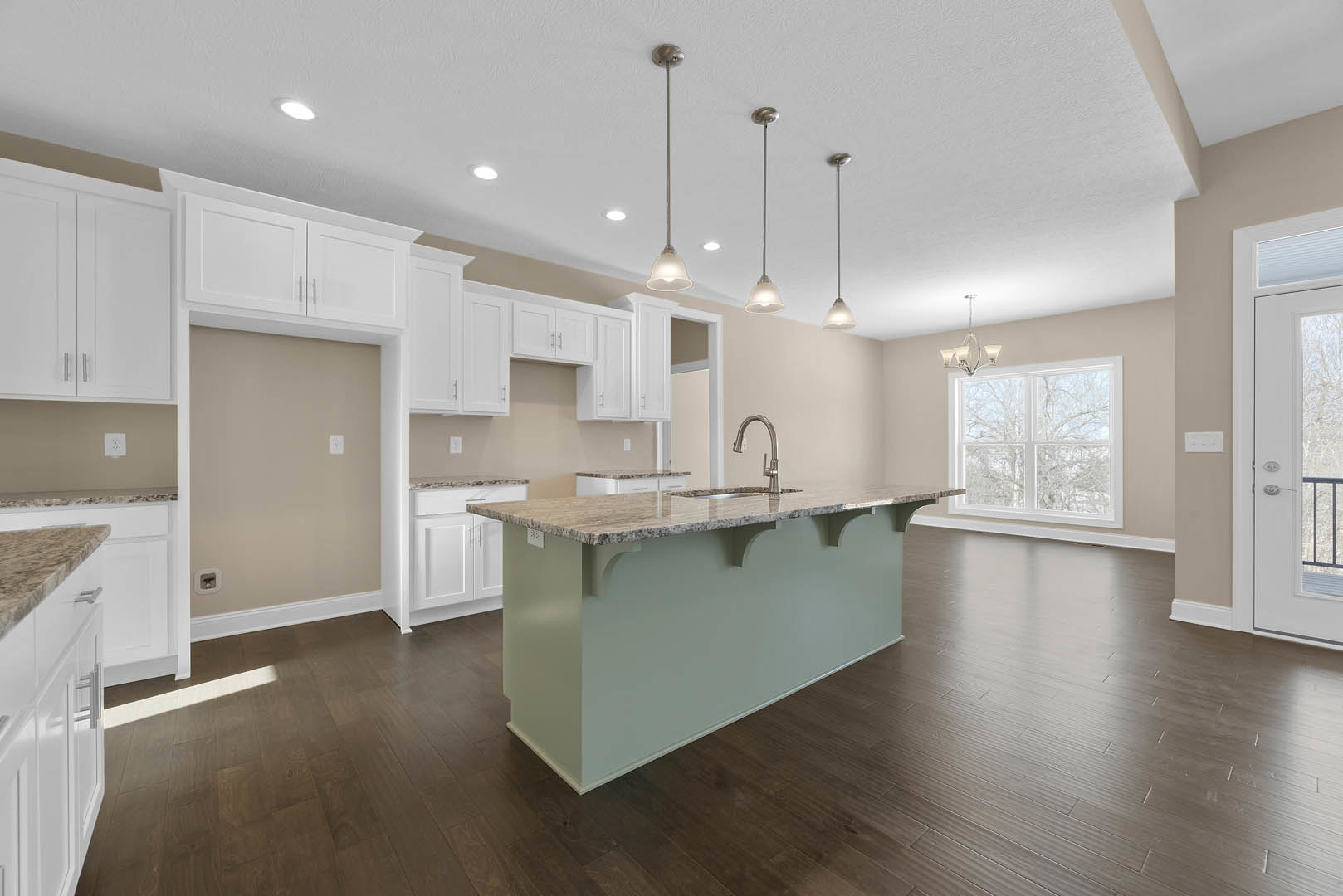 Kitchen with white shaker cabinets, central island featuring built-in sink, light stone countertops, stainless steel appliances, wide window overlooking leafy trees, white paneled