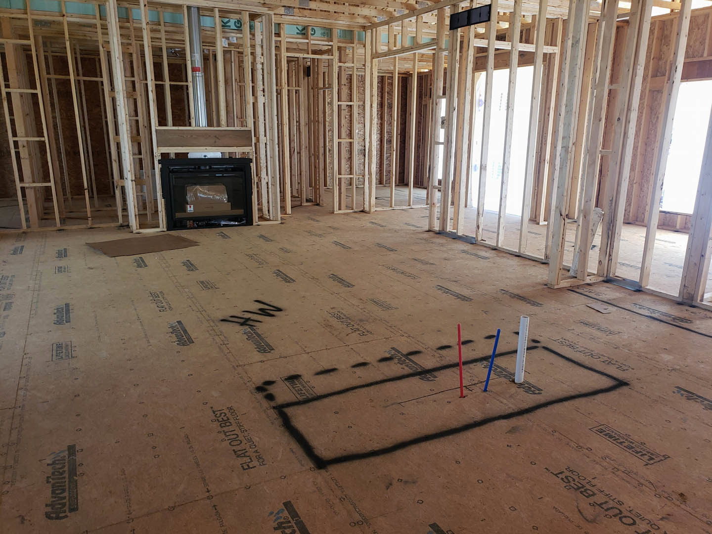 Unfinished living room with exposed wood framing, built-in fireplace, and construction materials scattered on subfloor