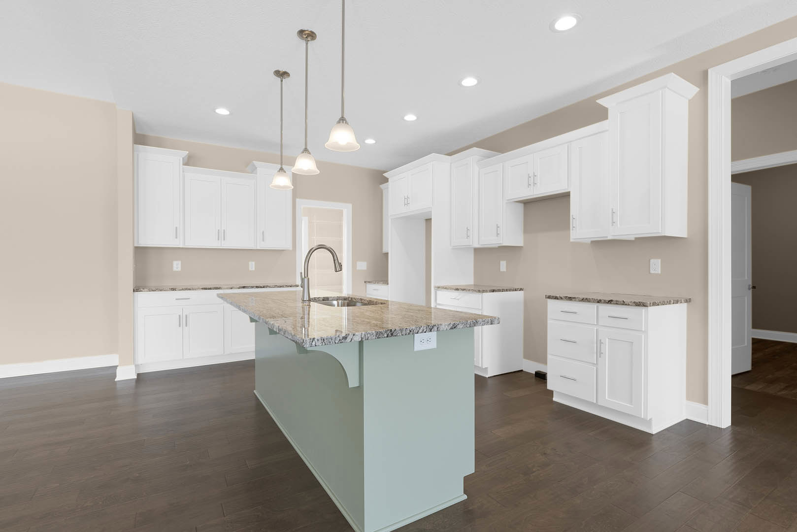 White kitchen with shaker cabinets, large central island featuring built-in sink and drawers, light stone countertops, stainless steel faucet, hardwood flooring, and recessed