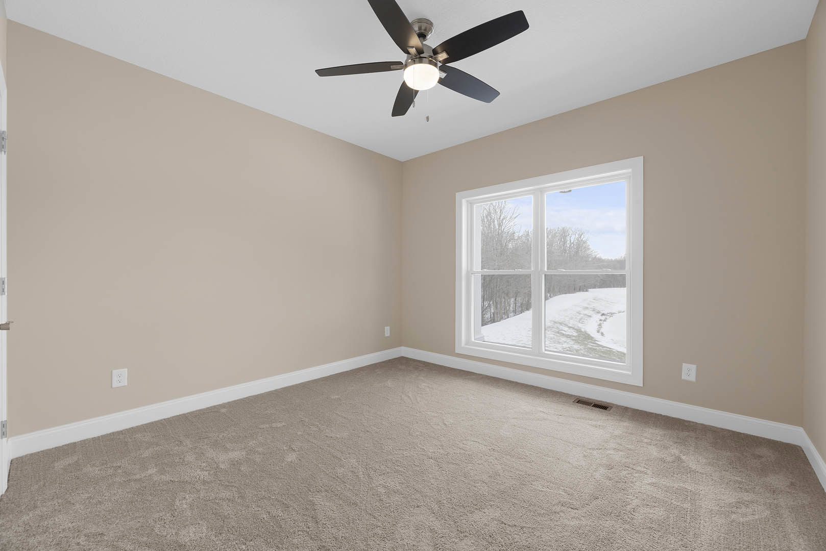 Carpeted room with white walls, ceiling fan with light fixture, large window overlooking snowy field, crown molding along ceiling.