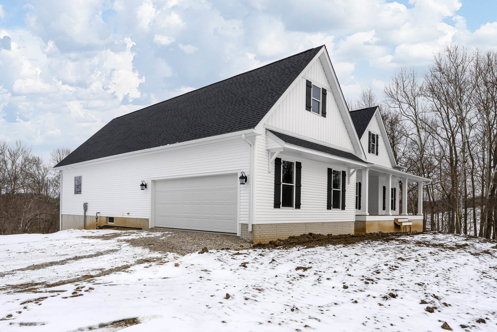 White house with attached garage, white siding and roof, white porch pillars, snow covering ground and trees, cloudy winter sky