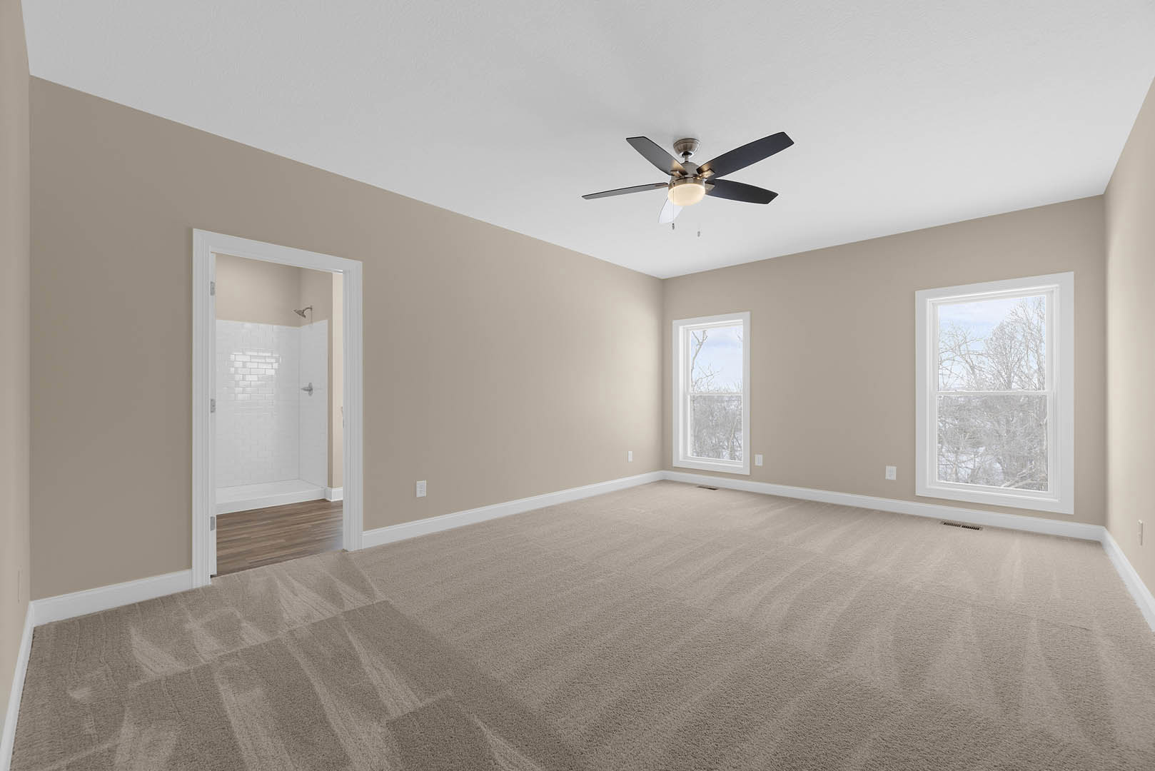 Carpeted bedroom with ceiling fan and light, window overlooking trees, adjacent bathroom featuring tiled shower and chrome showerhead
