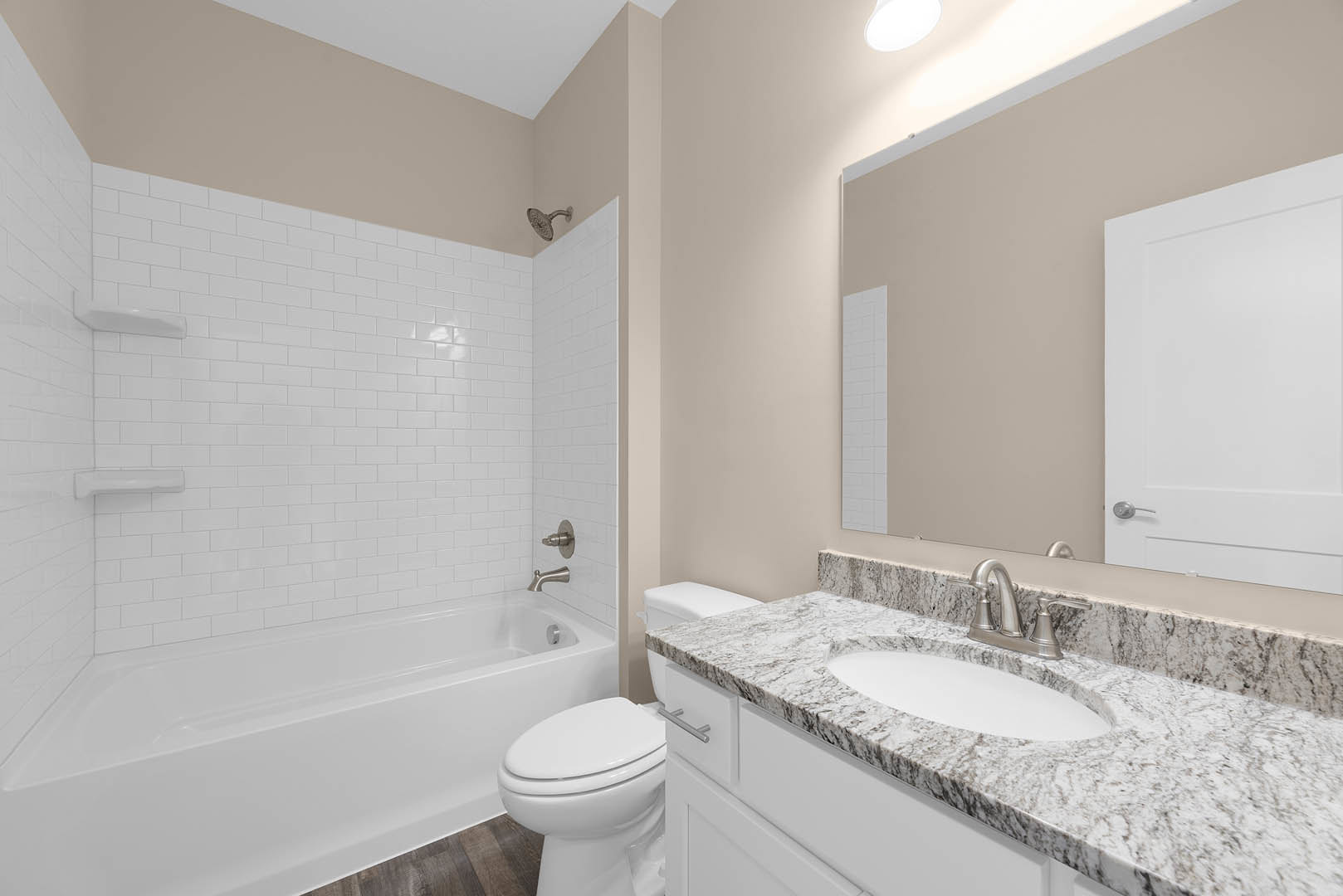 Marble countertop with undermount sink, freestanding white bathtub against tiled wall, chrome shower head, white door and frame, recessed lighting