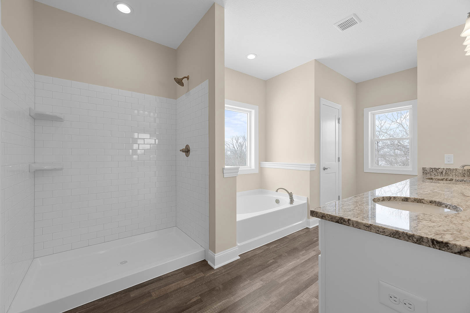 Bathroom with freestanding tub and glass-enclosed shower, large window overlooking trees, white door with silver knob, tiled walls, and stone countertop with sink and tap