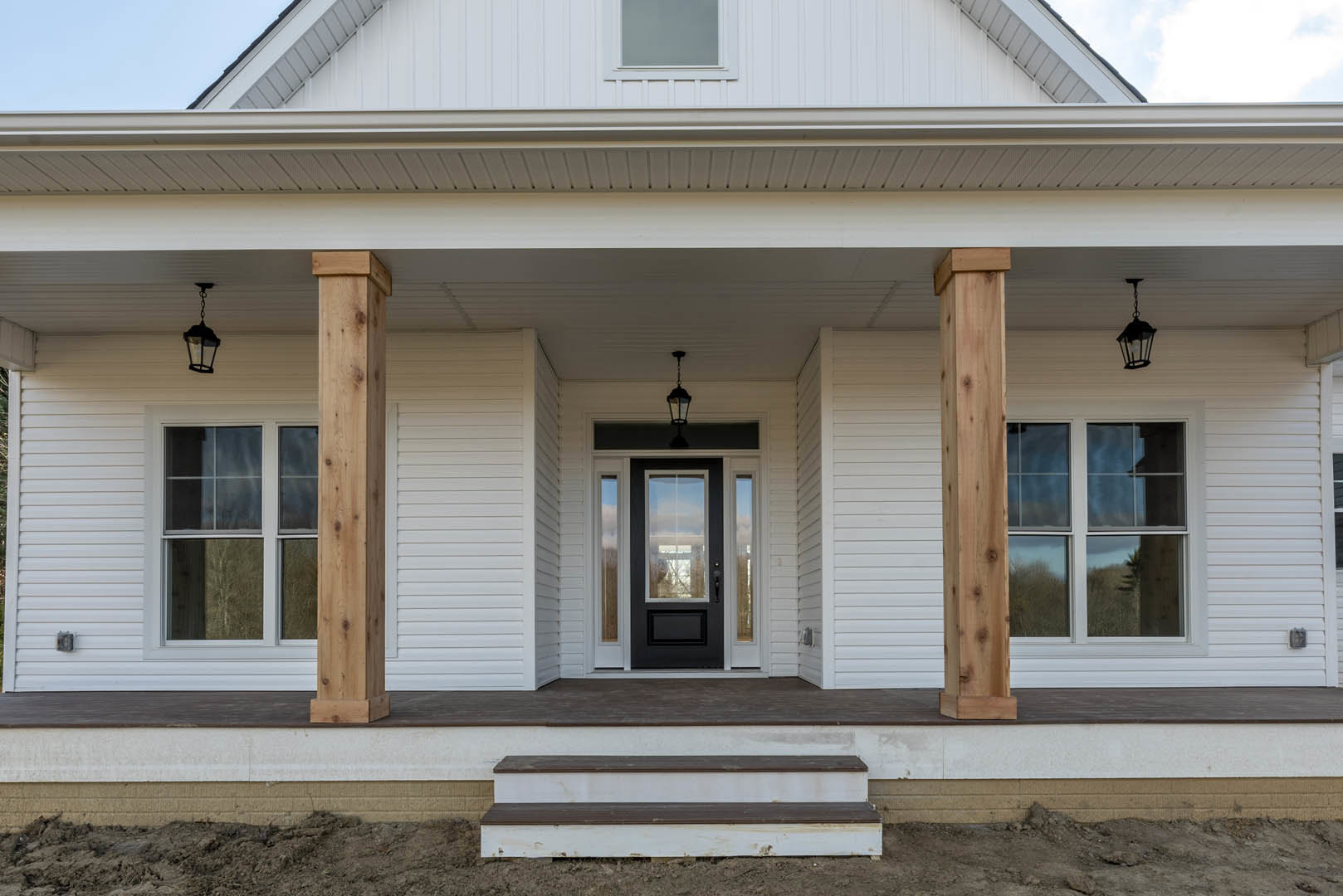 White siding house with covered front porch, black door, wood paneling accents, multiple sash windows, and wide stairs leading to entry